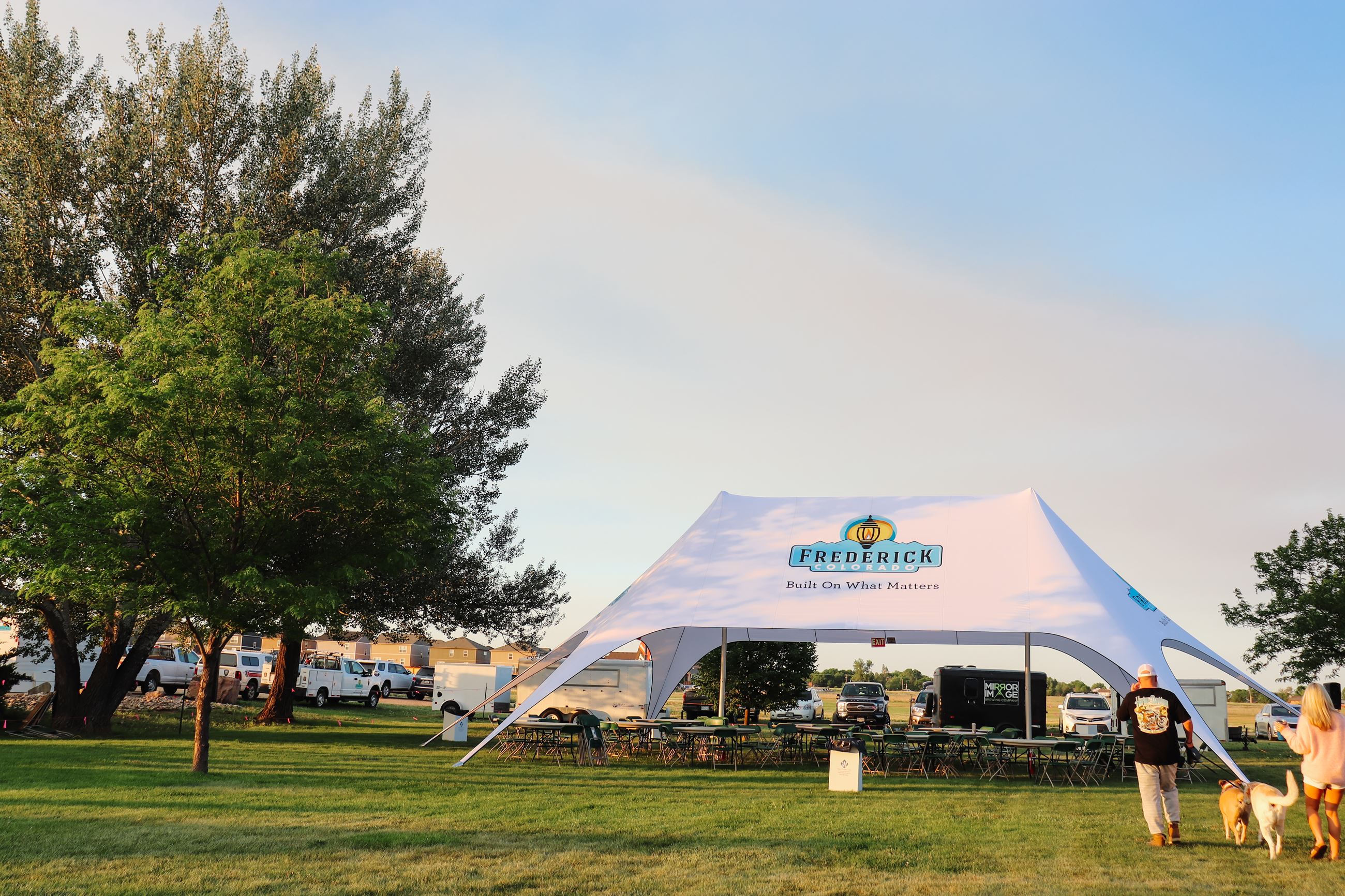 A Frederick tent with tables and chairs underneath it and a couple walk past with their dogs