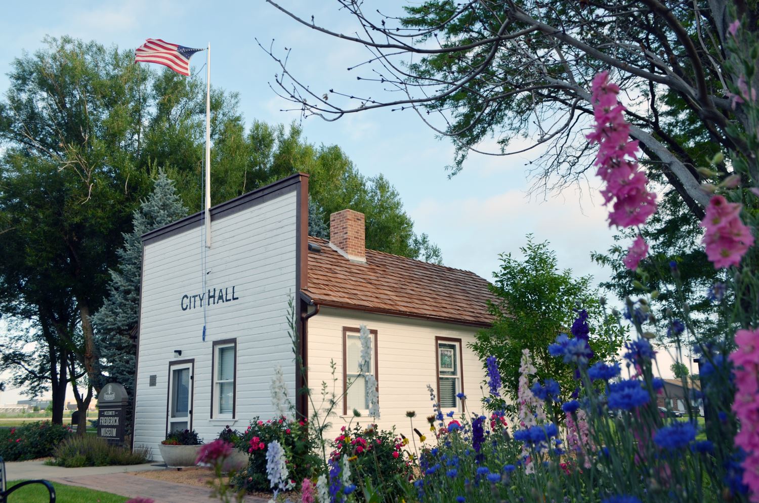 Historic Miner's Museum surrounded by blooming summer flowers, with the American flag