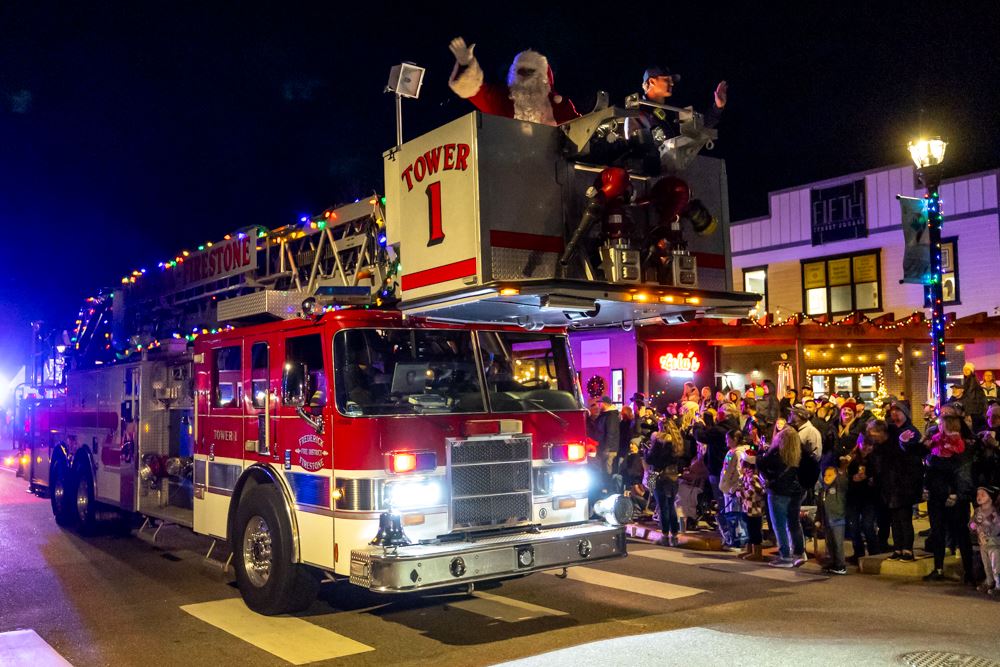 Santa and a firefighter wave from a fire truck during a holiday parade.