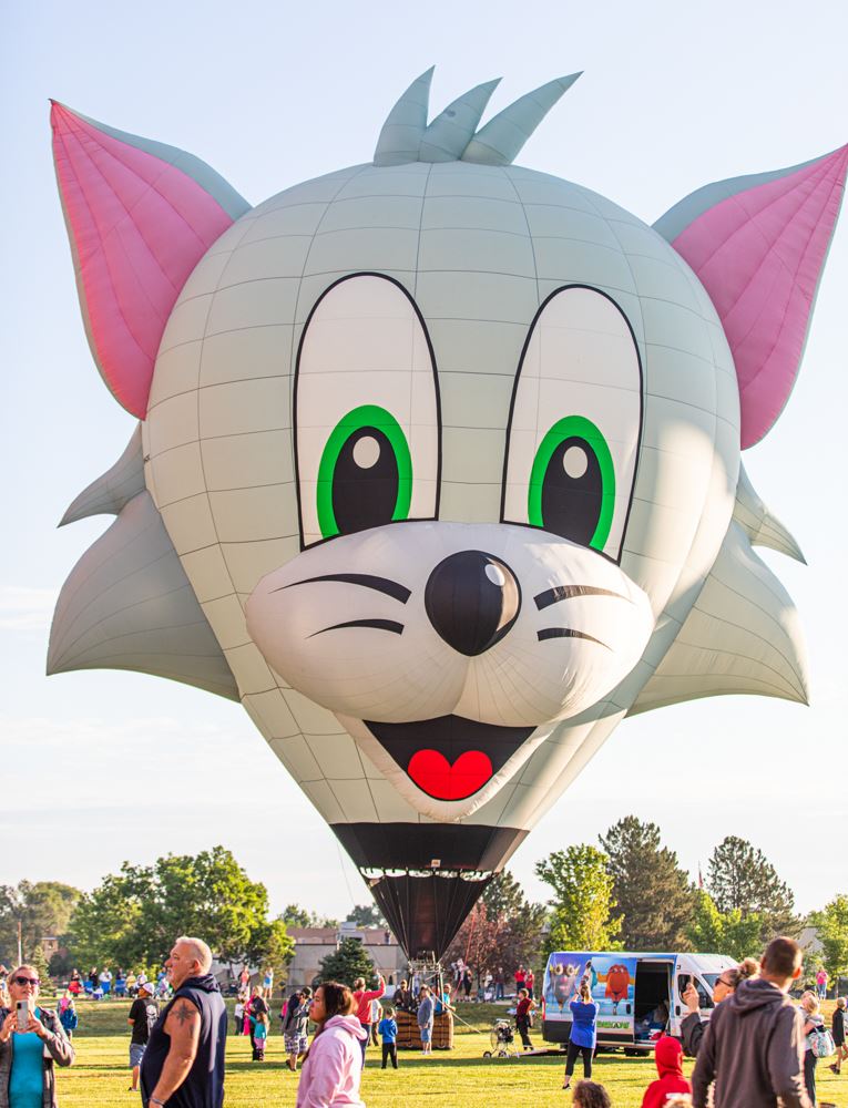 Large cartoon cat hot air balloon with a smiling face at a festival.