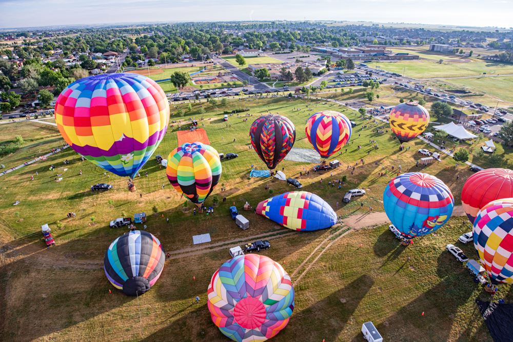 Colorful hot air balloons lift off from a grassy field during a festival.