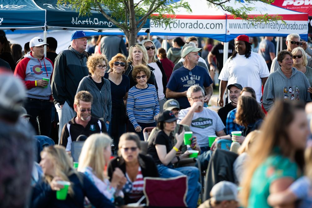 A crowd of people standing and sitting outdoors, enjoying a Frederick in Flight